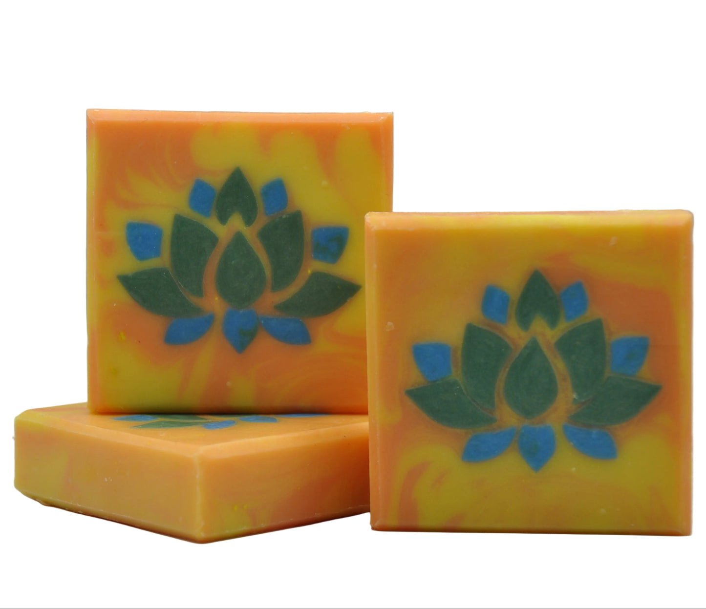Drei quadratische, handgefertigte Seifenstücke mit einem gelb-orange marmorierten Hintergrund und einem grün-blauen Lotusblumenmotiv, dargestellt auf einem strukturierten grauen Hintergrund.
