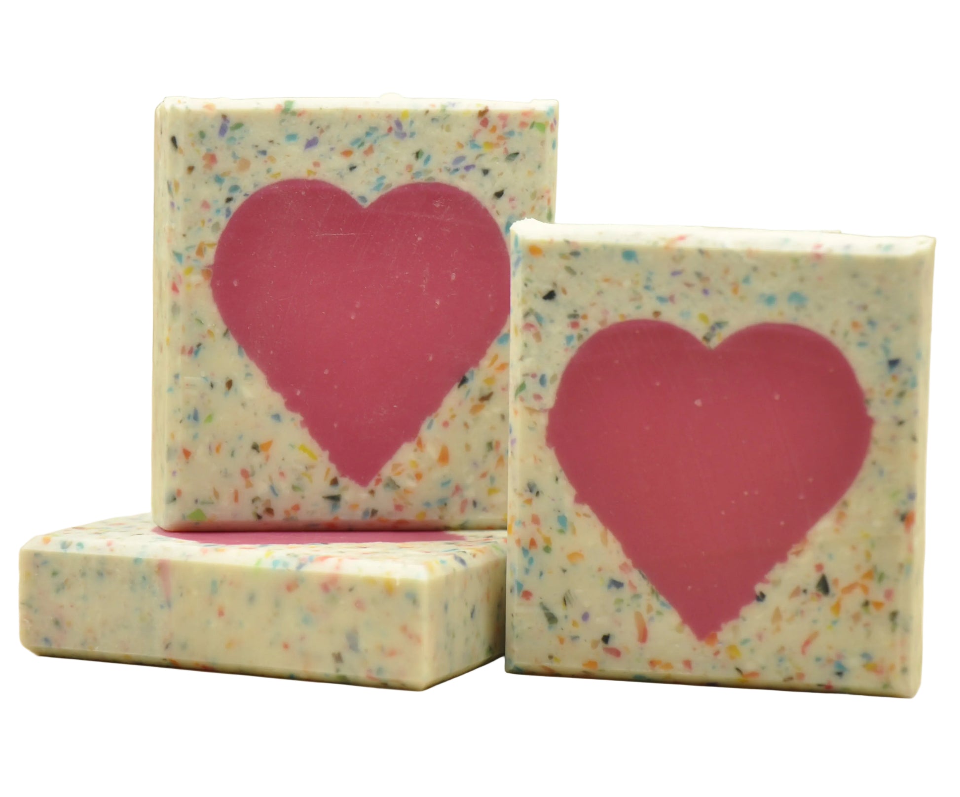 Drei Stücke handgemachte vegane Kaltverseifungsseife namens Love, mit cremig-weißer Basis, bunten Konfetti-Tupfern und einem kräftigen rosa Herz-Design, das durch den gesamten Riegel verläuft, duftend nach Zitrus und Eistee.